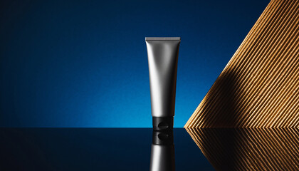 Silver Cosmetic Tube with Black Cap on Reflective Surface Against Blue and Gold Backdrop Keywords: cosmetic tube
