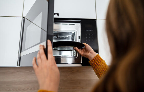 Woman placing a plate of food into the microwave.