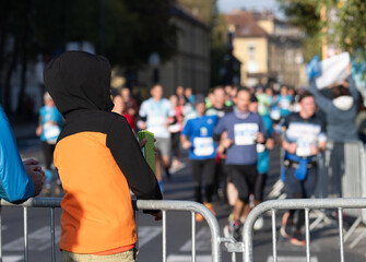 child in orange and black hoodie watching marathon runners running on street in ljubljana