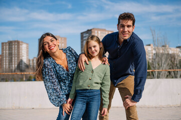 Cheerful parents with their daughter posing together under a clear sky