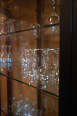 A close-up shot of sparkling clear glass wine glasses and various stemware displayed on transparent shelves inside a wooden cabinet.