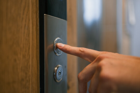 Human finger pressing silver elevator call button, signaling a wait for vertical transportation in a modern building, representing movement and transition