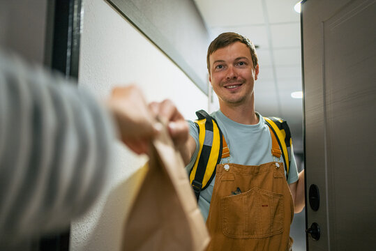 Male delivery person smiling, presenting a package to a customer at their home entrance, representing reliable e-commerce, express shipping, and convenient modern service industry