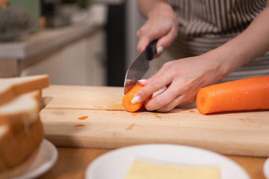 Close-up of hands slicing a fresh carrot on a wooden chopping board while preparing a meal