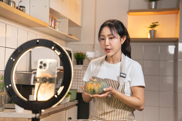 Happy Asian food vlogger talking and showing ingredients to her audience during a live stream cooking session