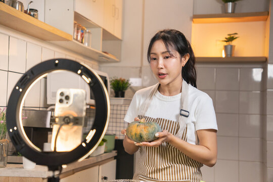 Happy Asian food vlogger talking and showing ingredients to her audience during a live stream cooking session