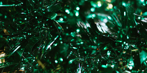 Macro abstract background of shiny dark green tinsel strands interspersed with bright green bokeh light spots.