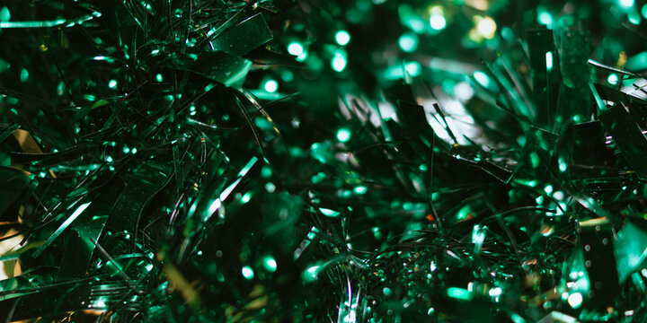 Macro abstract background of shiny dark green tinsel strands interspersed with bright green bokeh light spots.