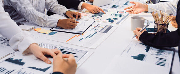 A diverse group of business professionals collaborates in a modern office setting, analyzing financial charts and graphs on documents for strategic planning and decision-making. SACTR