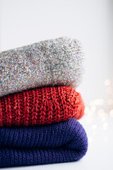 Stack of red, blue and shiny sweaters with blurred holiday lights.