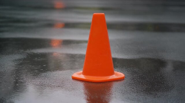 Safety orange cone on wet asphalt after rain. Plastic traffic cone. Road maintenance work. Close-up.