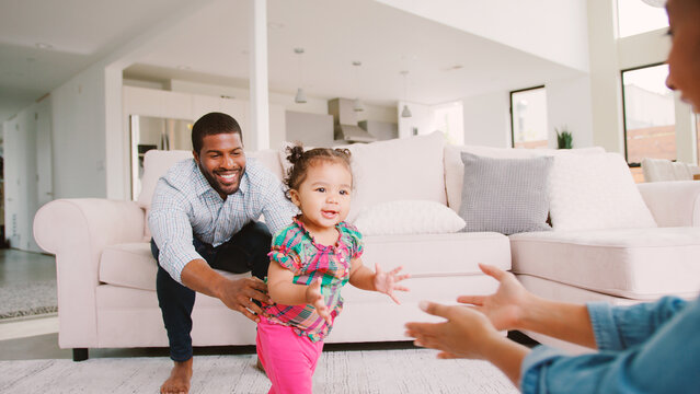 Family At Home Encouraging Baby Daughter To Take First Steps