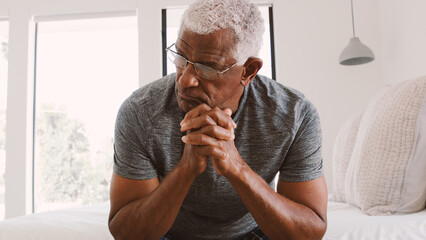Depressed Senior Man Looking Unhappy Sitting On Side Of Bed At Home With Head In Hands