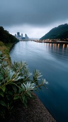 Obraz premium River scene at dawn, city skyline in the background. Lush greenery along the riverbank
