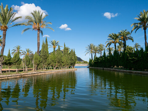 Symmetrical view of a narrow waterway in a manicured Mediterranean garden on a sunny day.