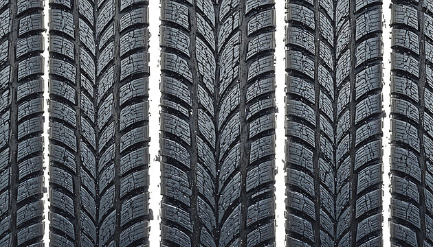 A close-up view of multiple car tires aligned vertically, showcasing symmetrical V-shaped tread patterns designed to channel water, enhance grip, and reduce hydroplaning in wet driving conditions.