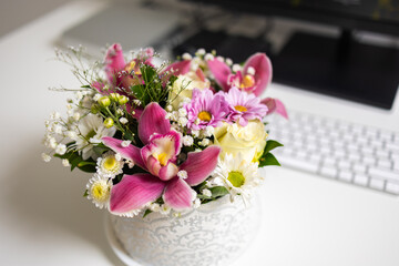 Elegant bouquet of pink orchids and daisies on white desk. Balance of work, beauty, and peaceful home ambiance.