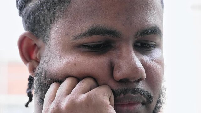 Close View Black Man With Braided Hair And Trimmed Beard Looking Down With Hand On Chin And Distant Expression In Peaceful Moment Of Introspection