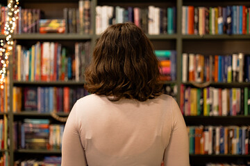 Woman looking at bookshelves with holiday lights in cozy bookstore evening. © sav_an_dreas
