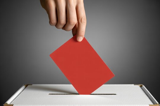 hand dropping red card into white box high contrast, voting concept in studio shot, civic decision making and democracy concept
