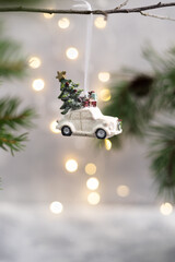 Christmas ornament shaped like a car, with a tree and gifts hanging from a branch, against festive bokeh lights in the background.
