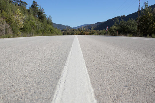 Low-angle view of a straight center line on an empty road with mountains ahead. Symbol of direction, focus and new horizons. - Powered by Adobe