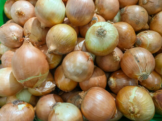 Close-up view of numerous fresh, unpeeled brown onions with golden skins, ready for sale in a grocery store or market.