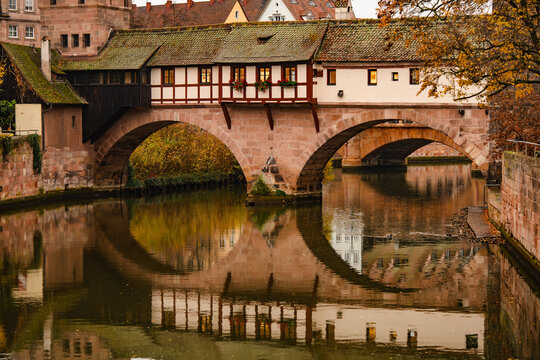 Historic Bridge And Medieval Architecture In Nuremberg: Traditional Half-Timbered Houses Reflected In Calm River Water On An Overcast Autumn Day