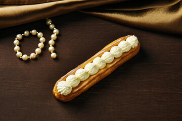 Delicious French Eclair With Cream And Pearl Necklace On Dark Wood