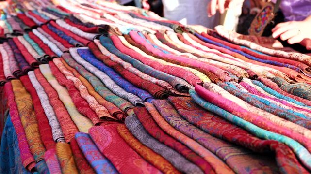 Person browsing colorful handcrafted Indian textiles and scarves at a bustling market in India