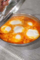 Sicilian-style eggs simmering in red tomato sauce. Traditional Italian eggs cooking in frying pan.