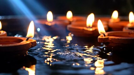 Lit earthenware oil lamps floating on water, reflections visible