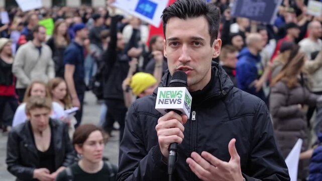 Reporter on crowded protest street, live coverage amid chanting crowd, signs and flags, handheld microphone, focused anchor delivering updates, urgent tone, gesturing to camera, urban square