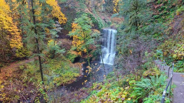 A beautiful view of the Lower South Falls, a distinct segmented waterfall flowing into a tranquil pool, framed by lush foliage turning vibrant autumn colors at Silver Falls State Park