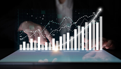 A business professional uses a touchscreen interface to interact with a digital financial graph, illustrating investment trends and data analysis in a modern workspace. Impute