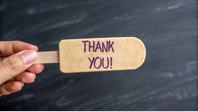 Young man's hand holding a handmade wooden cane with a thank you message on a wooden surface, ideal for warm and handcrafted backgrounds for headers and banners.