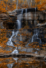 Fototapeta premium Smooth motion of flowing water against rough stone textures during fall season
