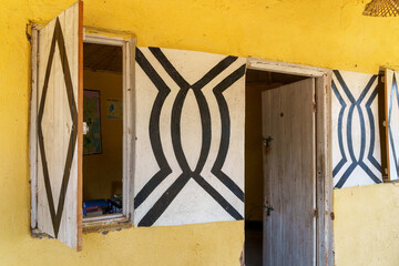 Building exterior yellow wall with wooden door and windows open and decorated with black and white pattern.