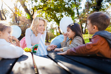 Female animator playing with a group of children at an outdoor birthday party at a table.