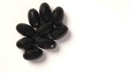 A close up of black capsules or pills on white background.