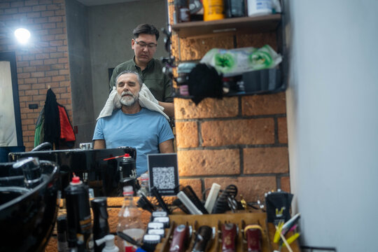 Barber drying male client’s hair with towel after washing in professional barbershop