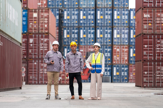 Team engineers wearing safety gear standing at container terminal, inspecting operations in stacked cargo container yard.