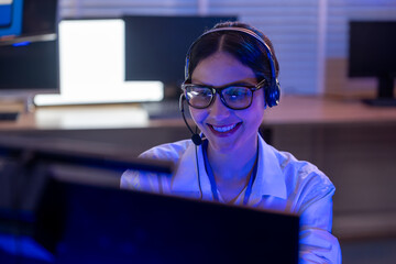 Female customer service agent wearing headsets support and assistance to clients working in call center office at night.