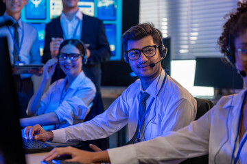 Man support and assistance call center at night in modern office. Diverse team of professionals customer service agent wearing headsets and monitoring computer working in dark control room.