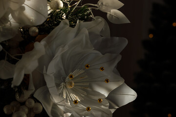 Elegant white Christmas flowers decorated with golden elements on a dark background. The flowers are softly illuminated, creating a festive and luxurious holiday mood