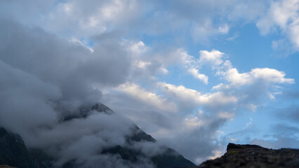 A dense, mid-level sky is dominated by a pattern of scattered, shattered white altocumulus clouds (sheep clouds) against patches of deep blue sky in Uttarakhand, india during trek to madhyamaheshwar.