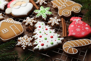 Tasty gingerbread cookies, spices and fir tree branches on cooling rack against brown background, closeup. Christmas treat