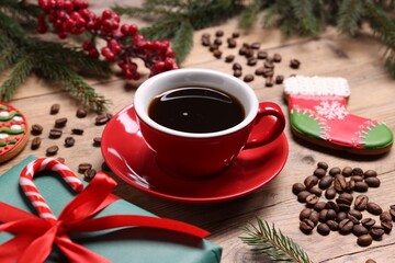 Aromatic coffee in cup, beans, gift box and Christmas decor on wooden table, closeup