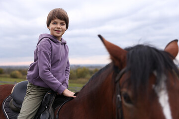 Fototapeta premium Equine assisted therapy. Little boy riding beautiful horse outdoors. Lovely domesticated pet