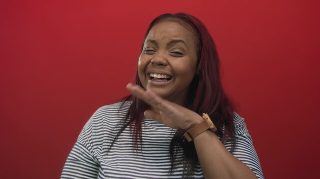African american woman face laughing with hand covering mouth in studio with bright red background; joy.